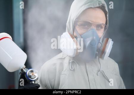 Femme spécialiste automobile travaillant avec un pistolet à peinture dans une cabine de peinture Banque D'Images