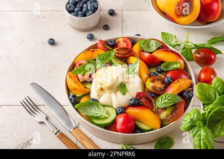 Salade de fruits et légumes d'été avec fromage burrata et basilic dans une assiette avec couverts pour un déjeuner ou un dîner savoureux. Plats végétariens Banque D'Images