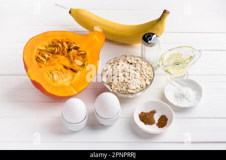 Ingrédients pour crêpes à la citrouille avec flocons d'avoine et banane : citrouille, banane, flocons d'avoine, œufs, huile végétale, épices, sel, poudre à pâte sur un dos blanc Banque D'Images