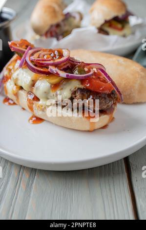 Cheeseburger sur pain de baguette française avec tomates, cornichons, oignons rouges et sauce barbecue maison. Banque D'Images