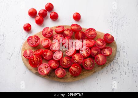 Panneau en bois avec tranches de tomates cerises sur fond bleu clair, vue du dessus. Cuisiner de délicieux plats faits maison Banque D'Images