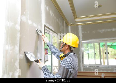 Un ouvrier appose un mur à l'intérieur d'une nouvelle maison de construction Banque D'Images