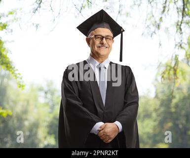Le doyen de l'université porte une robe de graduation noire et pose à l'extérieur avec des arbres dans le dos Banque D'Images