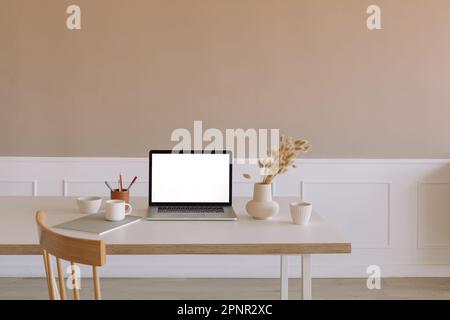 Gros plan d'un ordinateur portable ouvert sur une table à côté de fleurs séchées dans un vase, une tasse et des livres Banque D'Images