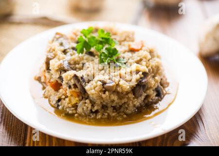 boulgour cuit avec des champignons, des carottes et des légumes dans une assiette, sur une table en bois. Banque D'Images