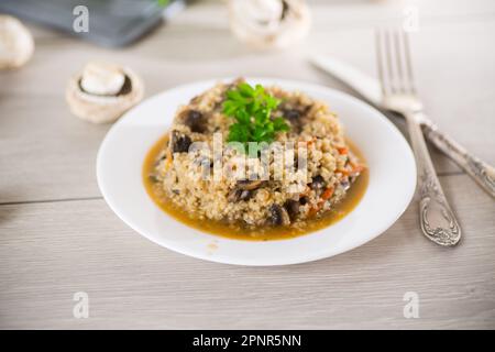 boulgour cuit avec des champignons, des carottes et des légumes dans une assiette, sur une table en bois. Banque D'Images