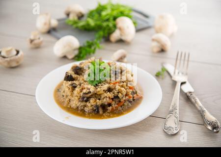 boulgour cuit avec des champignons, des carottes et des légumes dans une assiette, sur une table en bois. Banque D'Images
