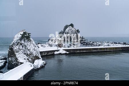 La côte rocheuse de la mer du Japon en hiver dans la préfecture d'Aomori, vue à partir d'un train sur la ligne Gono. Banque D'Images