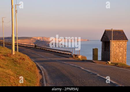 La route principale à travers Ogmore par la mer avec l'un des quatre abris de bus en pierre locale et les falaises s'étendant vers NOR point. Banque D'Images