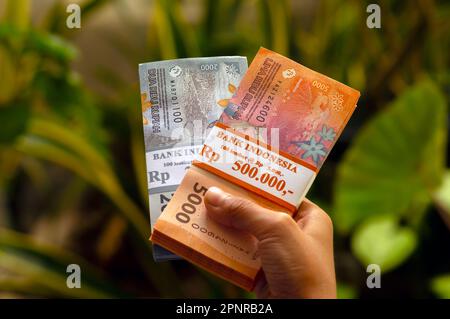 Un enfant asiatique tient l'argent indonésien dans un foyer peu profond. Concept d'épargne, de charité et de don Banque D'Images