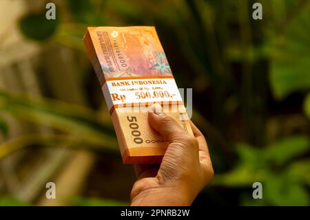 Un enfant asiatique tient l'argent indonésien dans un foyer peu profond. Concept d'épargne, de charité et de don Banque D'Images