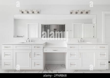 Une salle de bains avec une grande coiffeuse avec deux lavabos, sol carrelé de marbre et vue sur une cabine de douche carrelée de gris. Banque D'Images