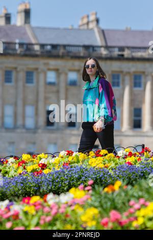 Bath, Royaume-Uni. 20th avril 2023. Avec le célèbre Royal Crescent de Bath en arrière-plan, une femme est photographiée en train de passer devant des lits de fleurs colouful dans le parc Royal Victoria. Les prévisionnistes prédisent que le temps sera plus frais et plus couvert dans les prochains jours. Credit: Lynchpics/Alamy Live News Banque D'Images