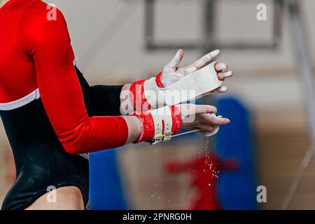 gros plan mains gymnaste femelle dans les poignées de gymnastique dans la craie de salle de gym, les barres inégales en cours d'exécution Banque D'Images