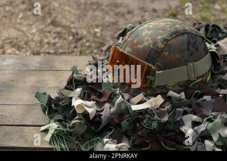 Un casque militaire avec des lunettes tactiques repose sur un filet de camouflage. Guerre russo-ukrainienne Banque D'Images