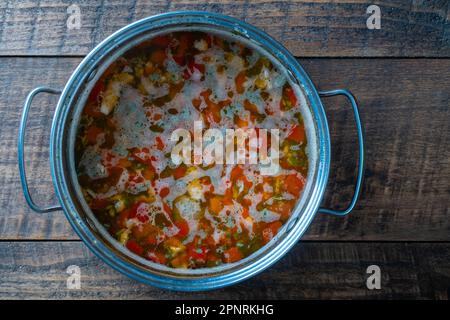 Soupe de poisson de saumon frais avec carottes, pommes de terre et poivrons rouges dans une poêle en métal sur une table en bois, gros plan. Un délicieux dîner se compose d'une soupe de poisson avec du salm Banque D'Images