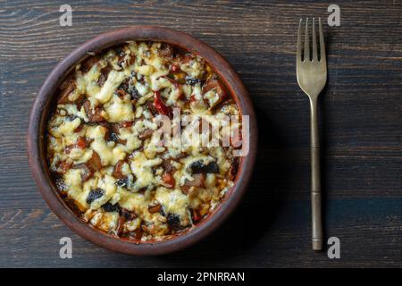 Purée de pommes de terre, carottes, oignons, tomates, pruneaux et fromage dans un bol en argile sur fond de bois, gros plan, vue de dessus Banque D'Images