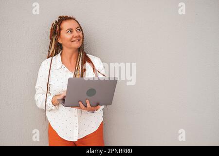 Une femme avec des dreadlocks tient un ordinateur portable ouvert dans ses mains et regarde vers le haut. Banque D'Images