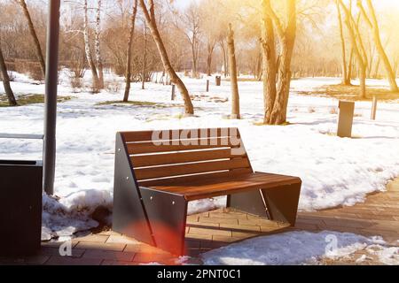 Banc en bois dans le parc de printemps. Soleil de printemps et neige dans le parc. Place pour se reposer pour une promenade. Marche le matin... Banque D'Images