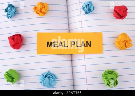 Une note papier avec les mots Meal Plan sur la feuille de cahier avec quelques boules de papier froissé colorées autour d'elle. Gros plan. Banque D'Images