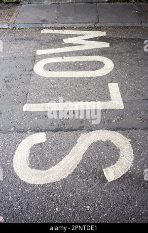 Le mot Slow en peinture blanche sur une surface de route en asphalte tarmac d'un angle inhabituel Banque D'Images