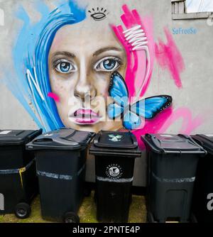 Scène de rue à Bristol Royaume-Uni avec graffiti d'une belle femme et un papillon bleu égorant une ligne rêveuse de poubelles Banque D'Images