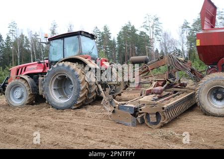 Un puissant tracteur diesel rouge avec une unité de semis connectée, une moissonneuse-batteuse à grandes roues plère la terre, sème les récoltes, effectue des travaux agricoles sur le terrain Banque D'Images