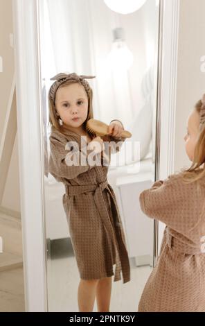 Une fille dans un manteau brun regarde à travers un grand miroir à l'appareil photo. Banque D'Images