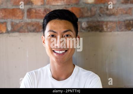 Portrait d'un homme d'affaires asiatique décontracté souriant contre un mur de briques au bureau Banque D'Images