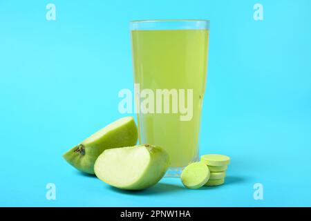 Verre de comprimé effervescent dissous dans de l'eau et des pommes sur fond bleu Banque D'Images