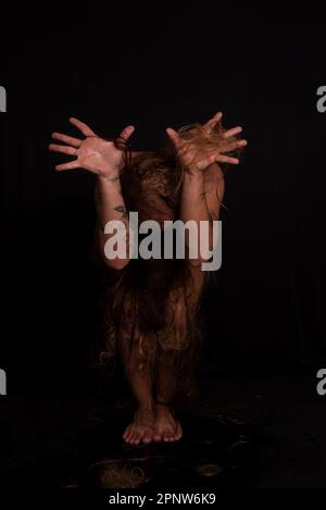 Jeune homme, acteur, portant bikini dans performance gorilla femme avec les cheveux partout dans son corps et expression de la douleur. isolé sur fond sombre. Banque D'Images