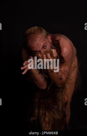 Jeune homme, acteur, portant bikini dans performance gorilla femme avec les cheveux partout dans son corps et expression de la douleur. isolé sur fond sombre. Banque D'Images