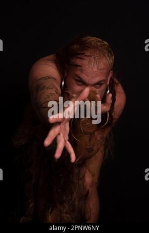 Jeune homme, acteur, portant bikini dans performance gorilla femme avec les cheveux partout dans son corps et expression de la douleur. isolé sur fond sombre. Banque D'Images