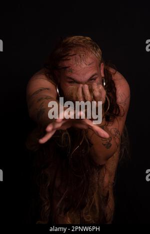 Jeune homme, acteur, portant bikini dans performance gorilla femme avec les cheveux partout dans son corps et expression de la douleur. isolé sur fond sombre. Banque D'Images
