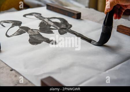 Un ancien calligraphe chinois écrit des caractères de pinceau, créant des œuvres de calligraphie chinoise. Traduction : le printemps vient, le dieu du vent arrive. Banque D'Images