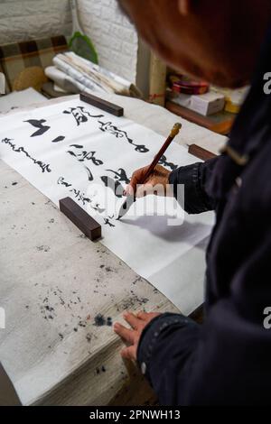 Un ancien calligraphe chinois écrit des caractères de pinceau, créant des œuvres de calligraphie chinoise. Traduction : le printemps vient, le dieu du vent arrive. Banque D'Images
