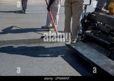 Les travaux sur route sont effectués par des ouvriers qui pelent du gravier noir pour la pose d'asphalte Banque D'Images