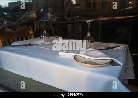 La salle à manger du restaurant est vide, l'éclairage est éteint. Nappe blanche, chaises en bois, verres à vin Banque D'Images