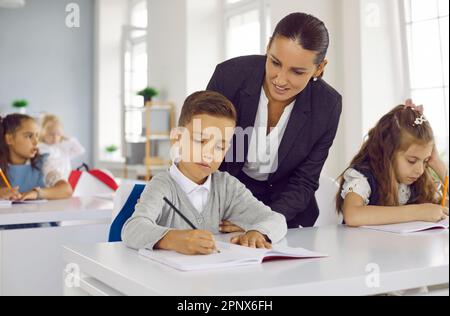 Une enseignante amicale et attentionnée aide un petit garçon avec une affectation scolaire en classe. Banque D'Images