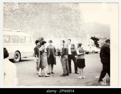 Vintage groupe de personnes rassemblées près d'un bus et d'une voiture dans un endroit extérieur pittoresque. Une photographie en noir et blanc capture un moment dans le temps avec plusieurs Banque D'Images