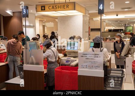 Avril 2023, les clients paient les provisions à la caisse dans une salle de cuisine de Tokyo à Shinjuku, le personnel porte des masques, Japon, Asie Banque D'Images