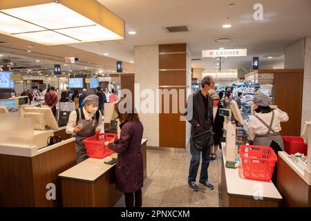 Avril 2023, les clients paient les provisions à la caisse dans une salle de cuisine de Tokyo à Shinjuku, le personnel porte des masques, Japon, Asie Banque D'Images