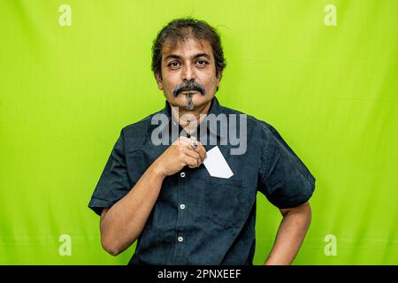 Homme d'affaires habillé avec élégance dans une chemise noire au visage souriant, tient et met une carte de crédit/débit vierge dans la poche, sur fond vert Banque D'Images