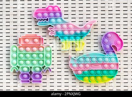 Vue de dessus des jouets anti-stress Pop IT colorés de différentes formes placés sur une table en osier en plastique Banque D'Images