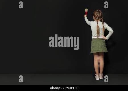 L'enfant fille se tient avec son dos et peint sur le tableau noir de l'école. Retour à l'école, éducation, étudiant, élève Banque D'Images