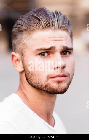 Jeune homme blond barbu dans un t-shirt dans la rue de la ville d'été Banque D'Images