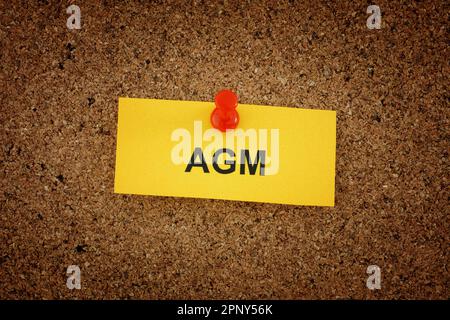Une note de papier jaune avec les mots AGM (Assemblée générale annuelle) sur elle accrochée au panneau de liège. Gros plan. Banque D'Images