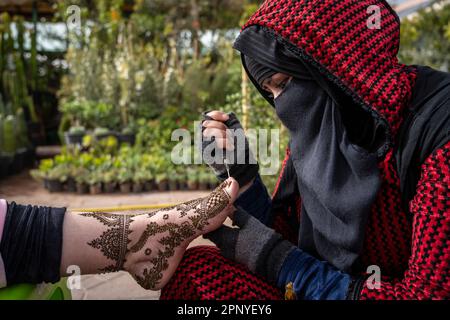 Femme musulmane décorant le pied d'un client avec henné sur la place Jemaa el-Fnaa à Marrakech. Banque D'Images