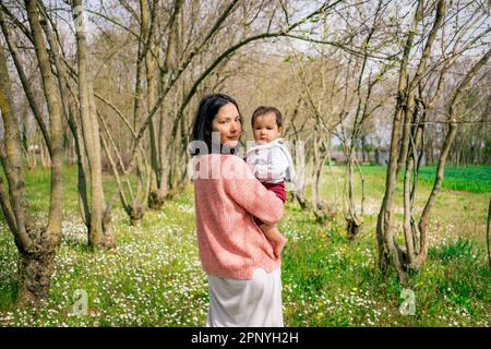mère heureuse et petite fille debout ensemble sous un arbre dans la campagne, souriant avec amour et affection. Un portrait parfait de la famille bondin Banque D'Images