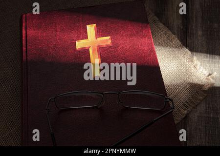 Un rayon de soleil dur tombe sur un vieux livre rouge. Sunbeam dans l'obscurité, sur un livre. Gros plan. Vieux livre rouge Banque D'Images